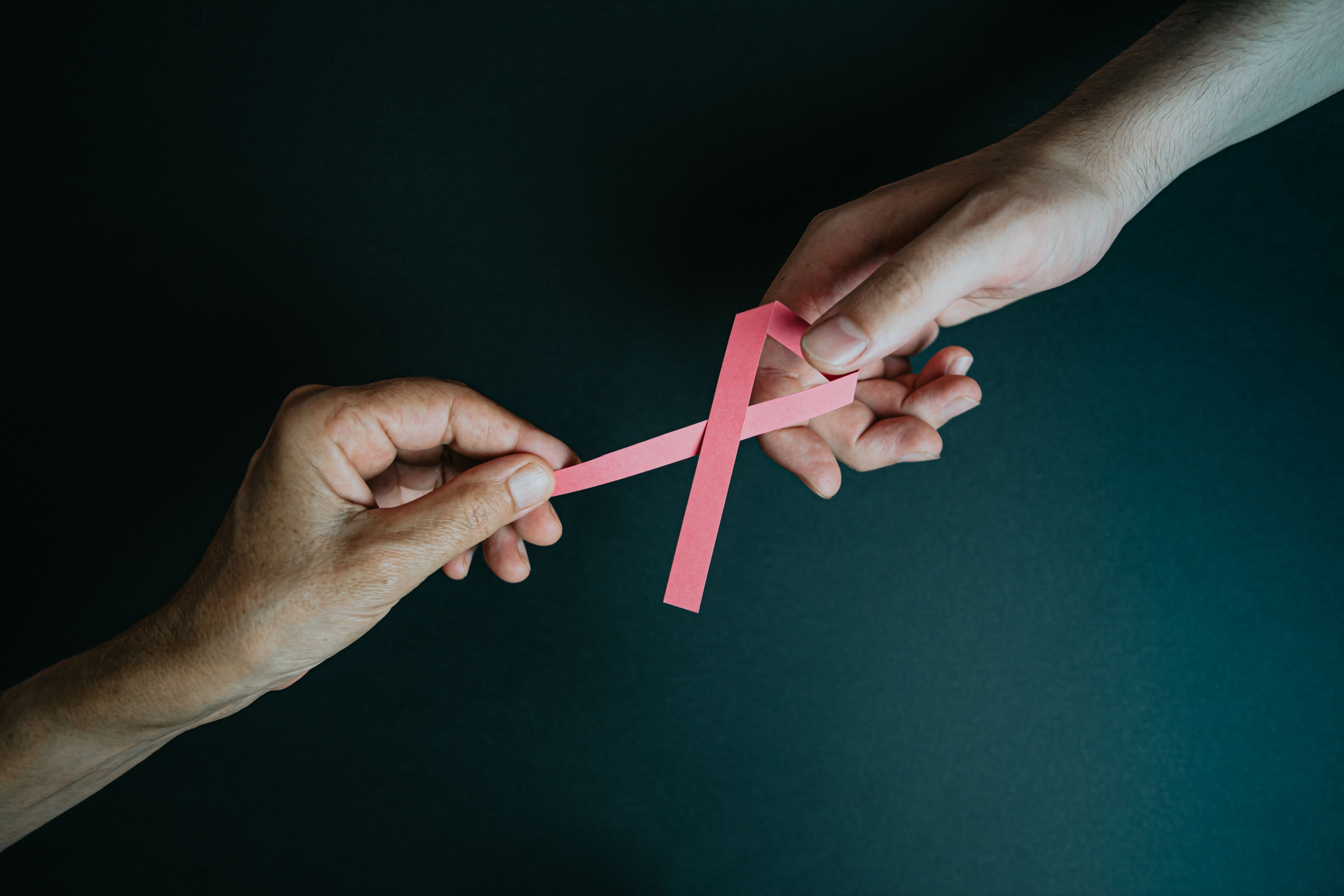 A hand passing a pink ribbon to another hand.