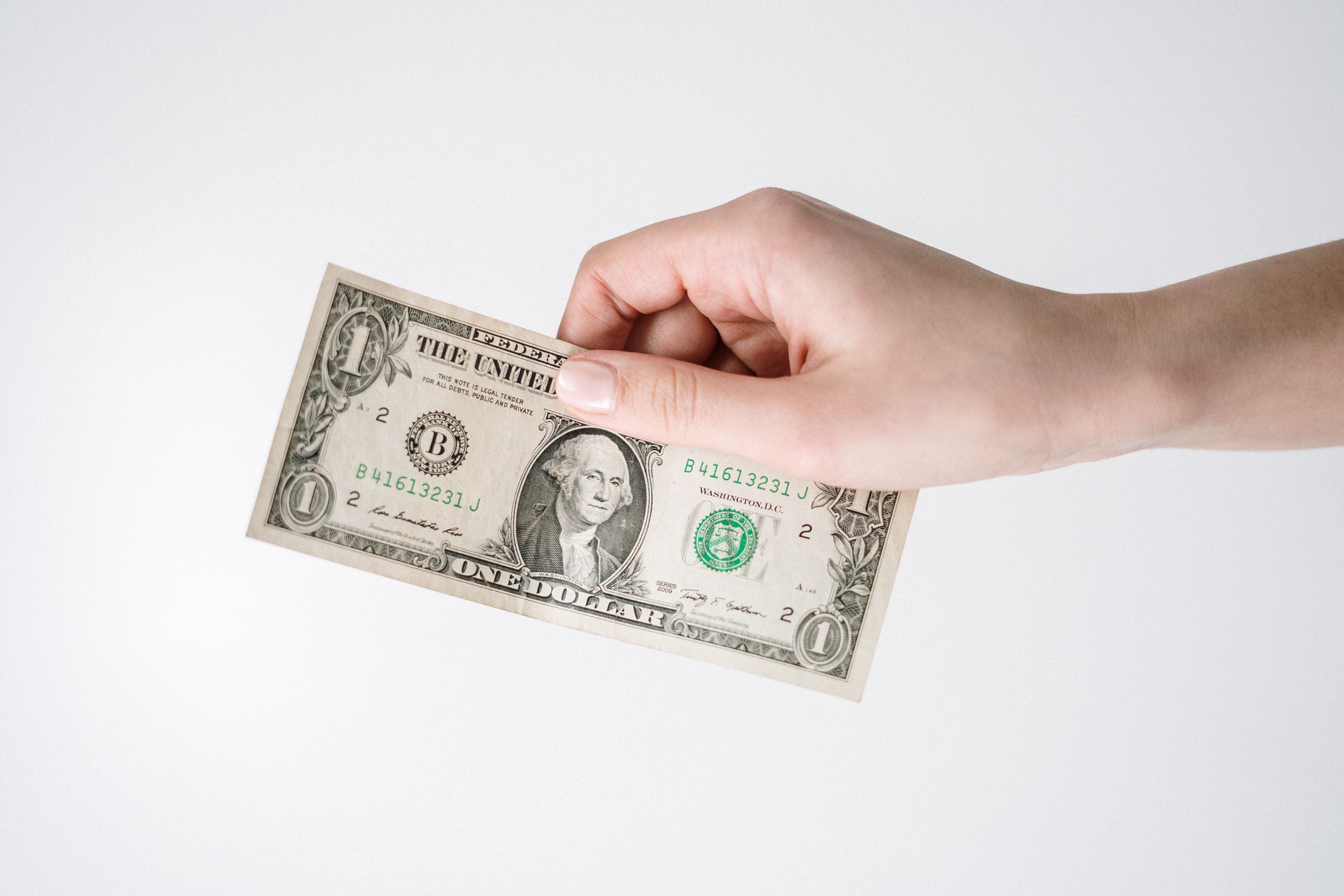 A hand reaching out holding a dollar bill to give away.