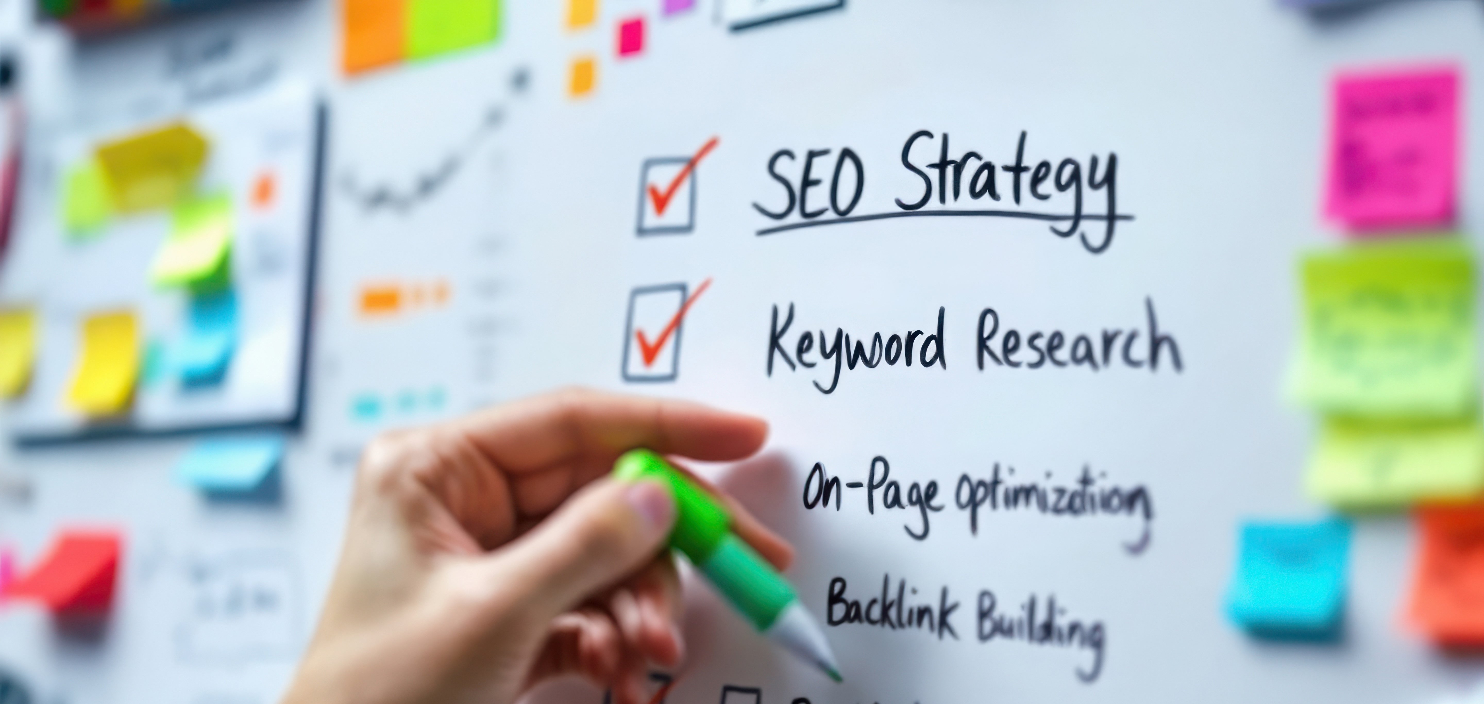 A whiteboard with different colored post-it notes stuck to it, and a checklist in the center that is in focus and reads "SEO Strategy, Keyword Research, On-Page Optimizing, Backlink Building"