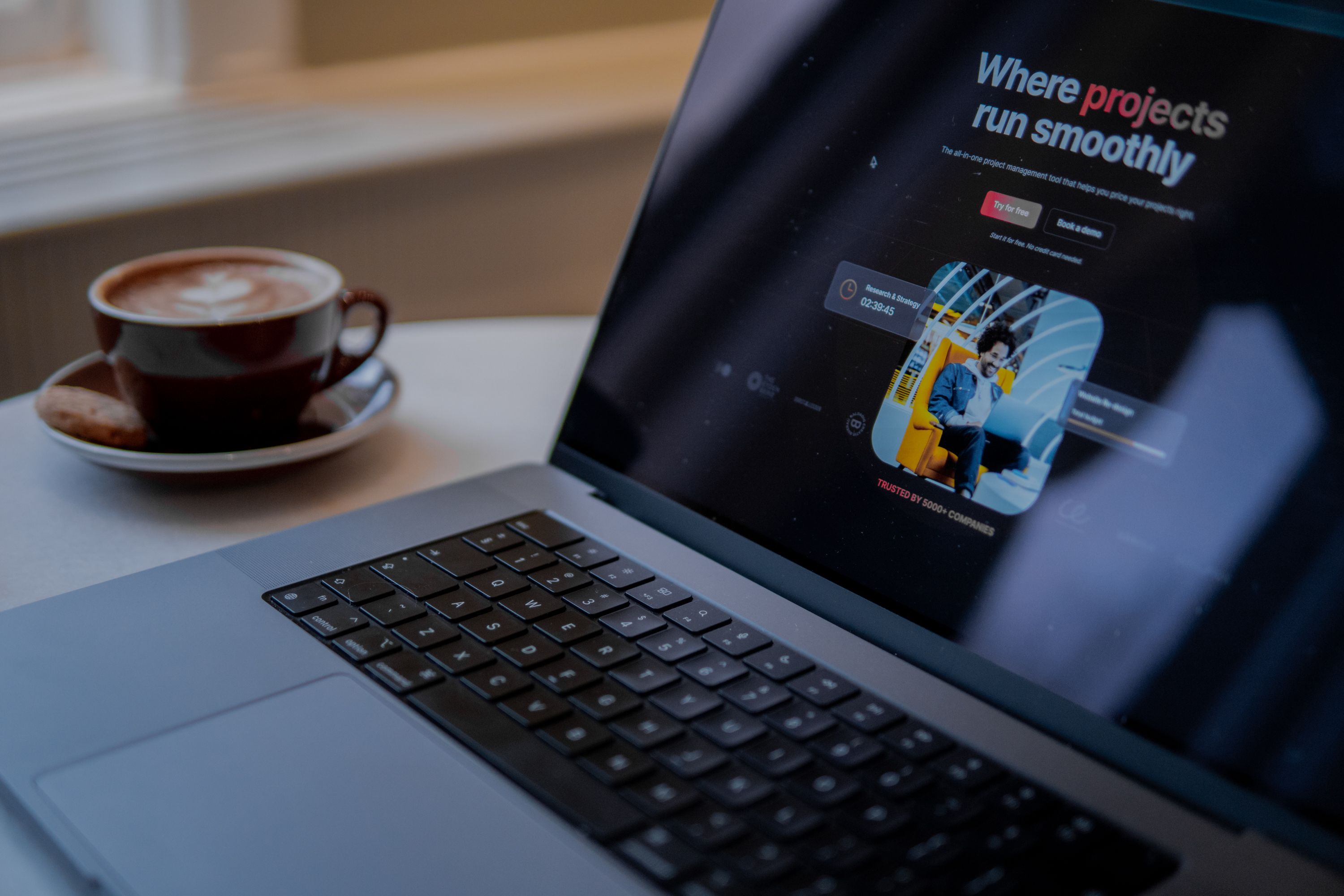 A laptop sitting on a table next to a cup of coffee with a B2B website on the screen that is selling project management software.